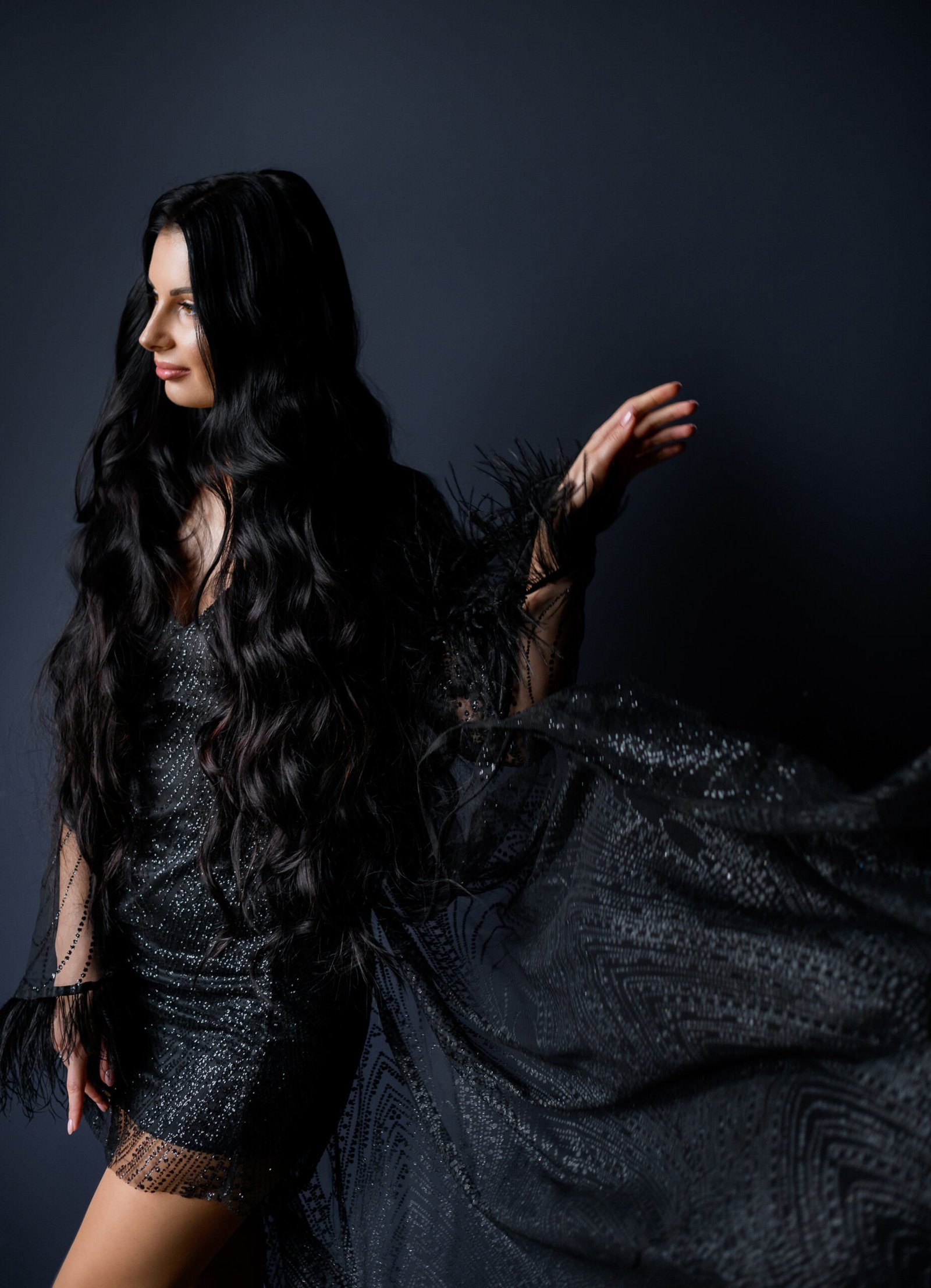 Attractive longhaired brunette girl dressed in luxury black dress on the black background